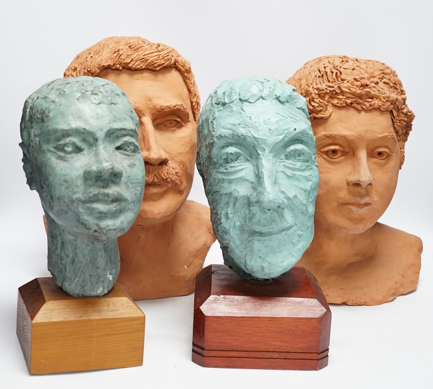 Four art pottery sculpted heads on stands, two terracotta and two painted verdigris green, largest 34cm high